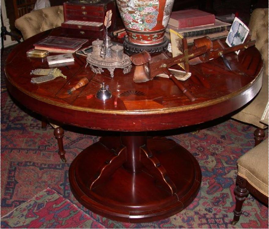 Inlaid teakwood circular table with geometric motifs in 'rising sun' design supported on cylindrical post with four scalloped braces at the top and circular, molded base