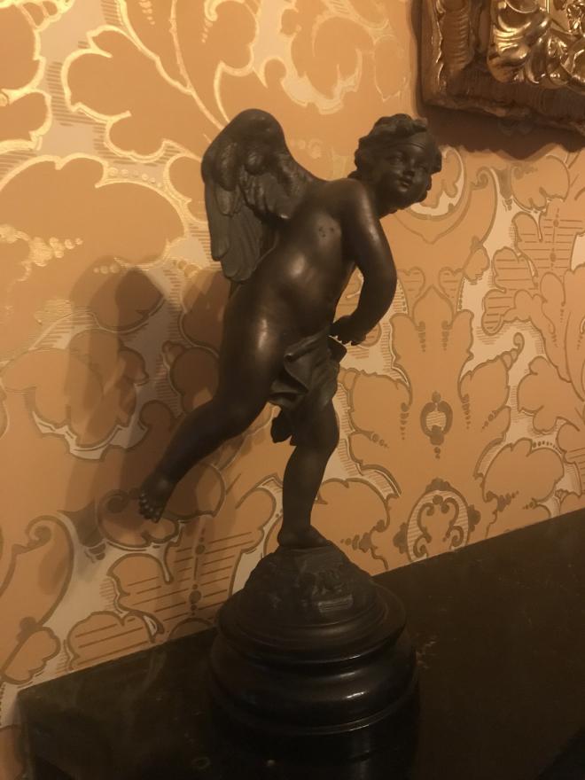 Winged naked cupid stand as if he has just thrown an arrow looking off to his right. A cloth wraps around his body to cover his private area.