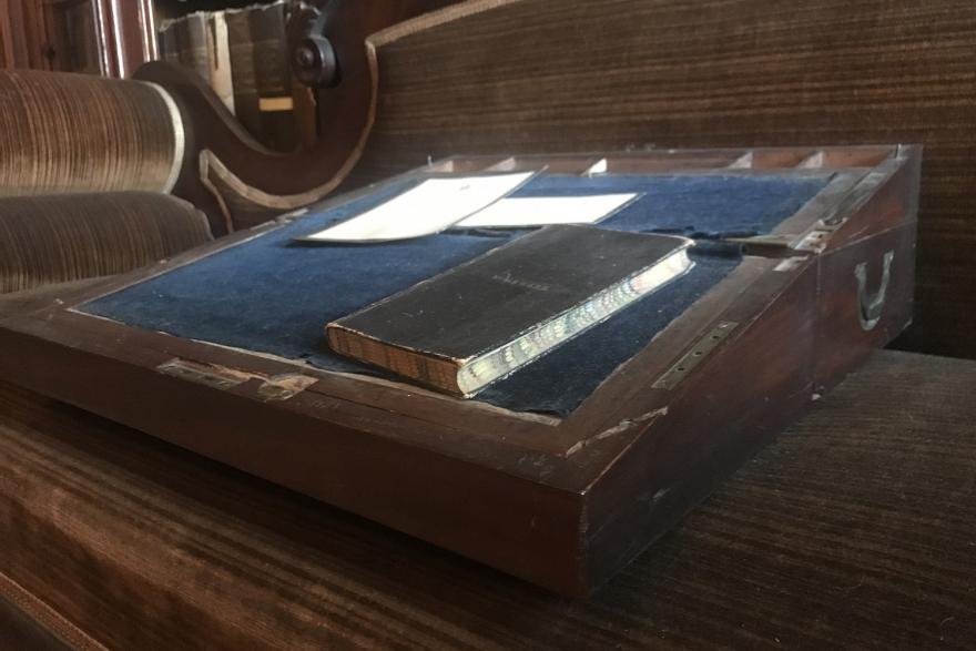 Portable, folding writing desk of bird's eye and tiger maple.  Door on top inside may be let down to disclose section for correspondence.  Writing desk in center with 6 sections at top.  Lower drawer with brass knob.  Blue velvet inside.