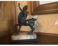 clean shaven bronze centaur carrying a club and skin of a fox over one arm while the other is raised up as he stands on a rectangular marble base