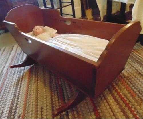 A cherry cradle with solid bottom. Headboard higher, but same design as footboard. Open hand grips on each side. Short rockers.